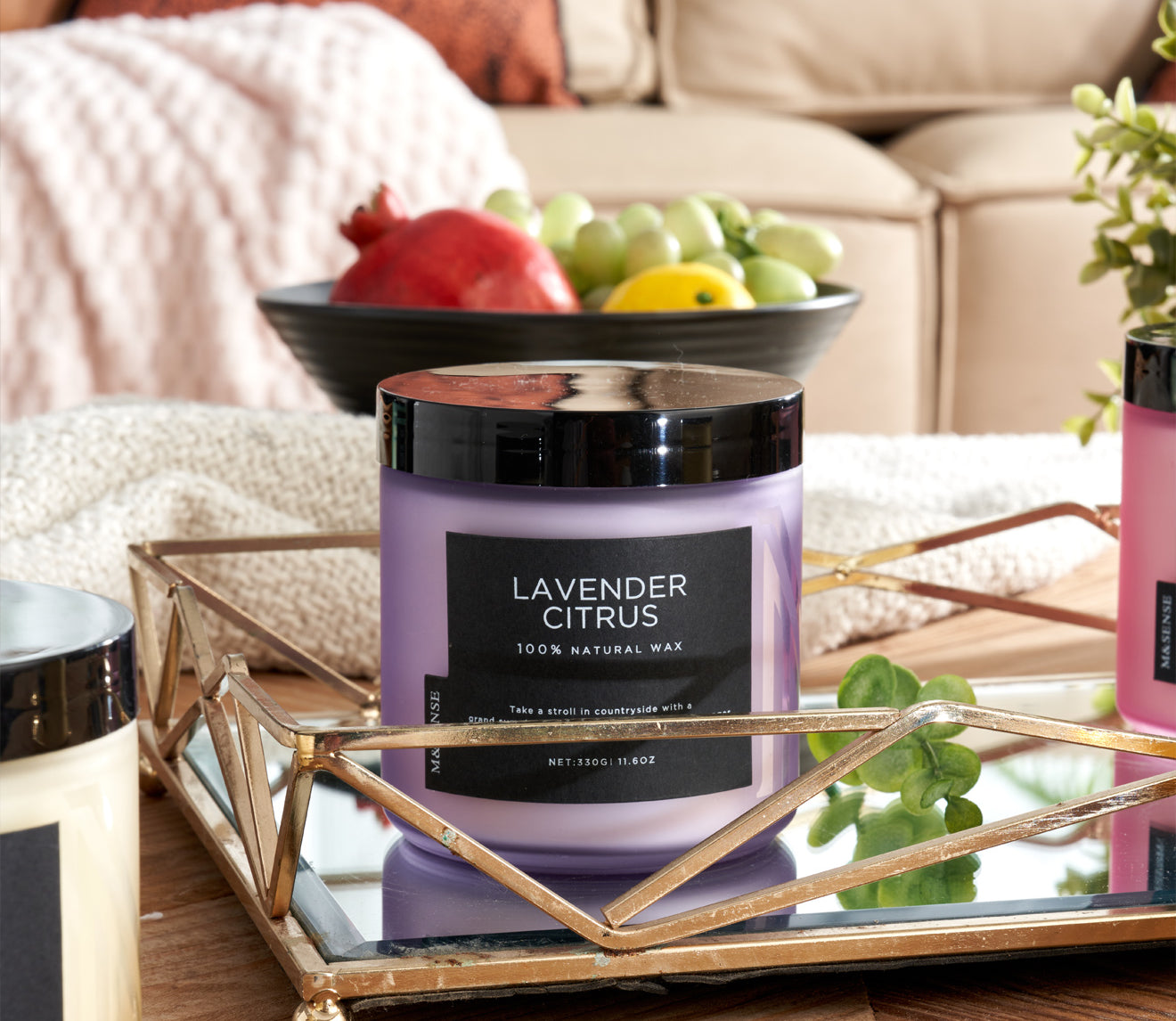 Lavender Citrus candle on a coffee table next to a fruit bowl, enhancing a cozy living room with a sofa.