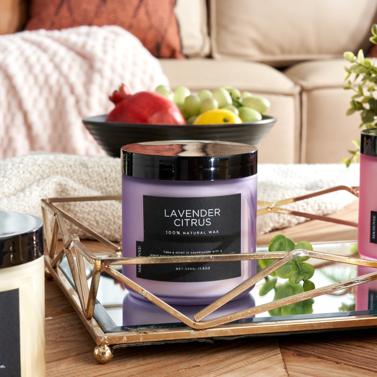 Lavender Citrus candle on a coffee table next to a fruit bowl, enhancing a cozy living room with a sofa.