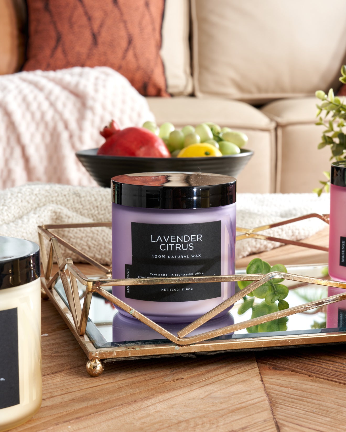 Lavender Citrus candle on a coffee table next to a fruit bowl, enhancing a cozy living room with a sofa.