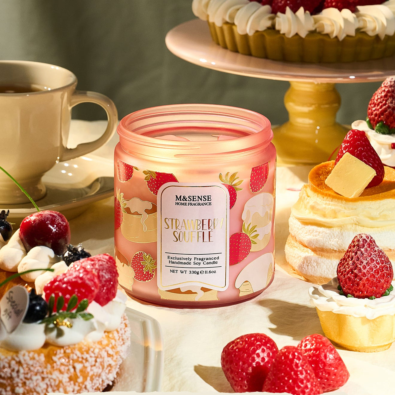 Candle with strawberry design surrounded by desserts and a cup on a light background