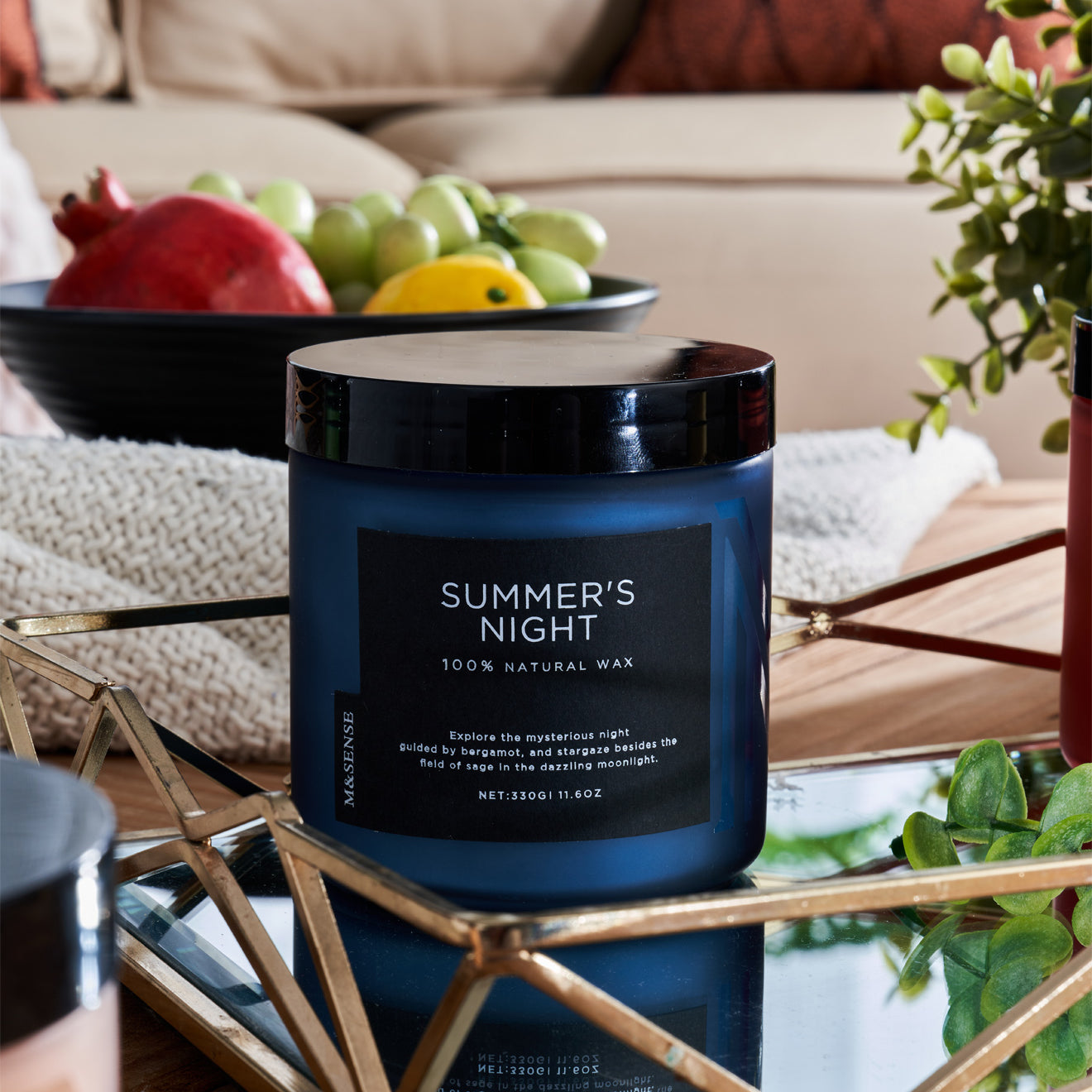 Summer's Night candle on a table with fruit bowl, enhancing a cozy living room with sofa.