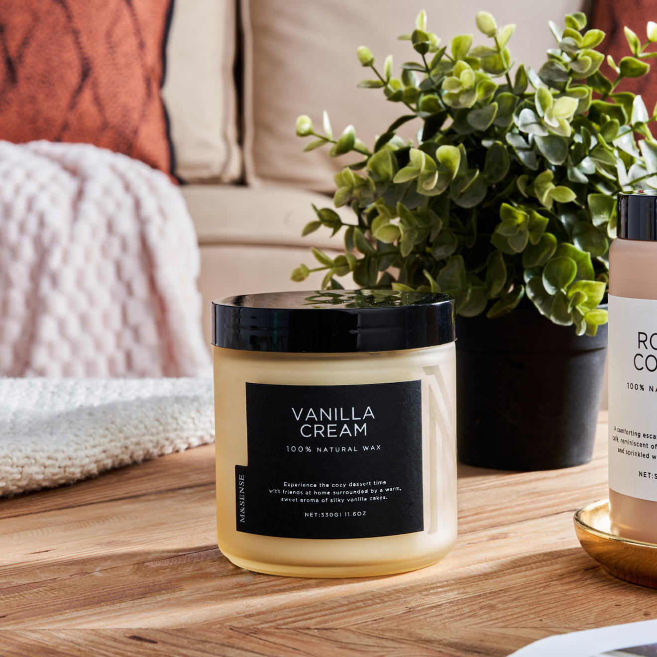 vanilla cream scented candle on wooden table with plant and cozy home decor.
