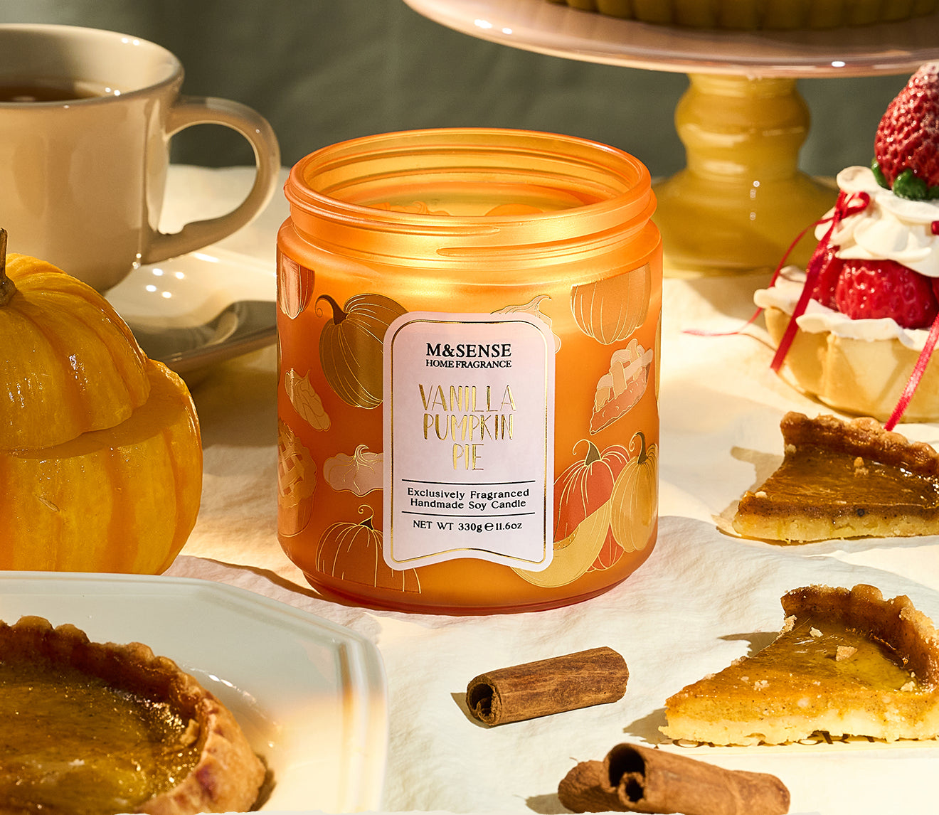 Orange candle labeled 'Vanilla Pumpkin Pie' on a table with desserts and a cup.