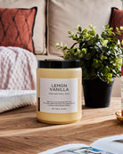Lemon Vanilla scented candle on a wooden table with a green plant, against a sofa background.