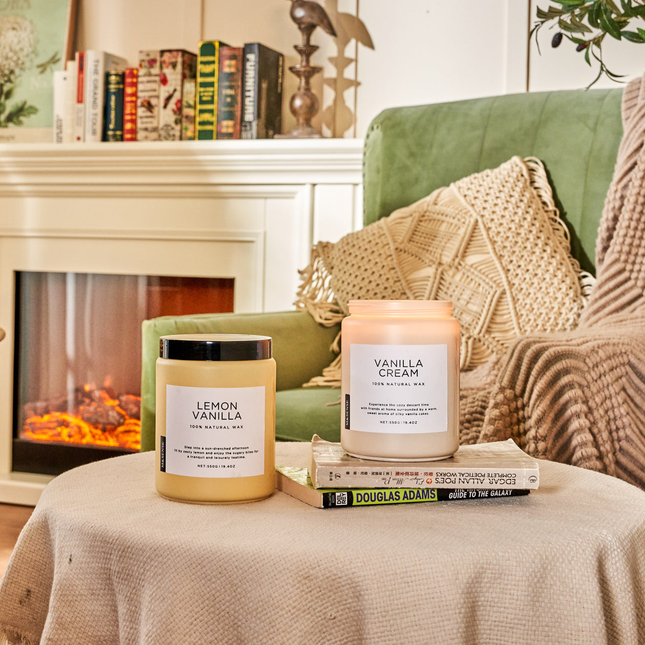 Two scented candles on a draped round coffee table, in a living room with sofa and bookshelf.