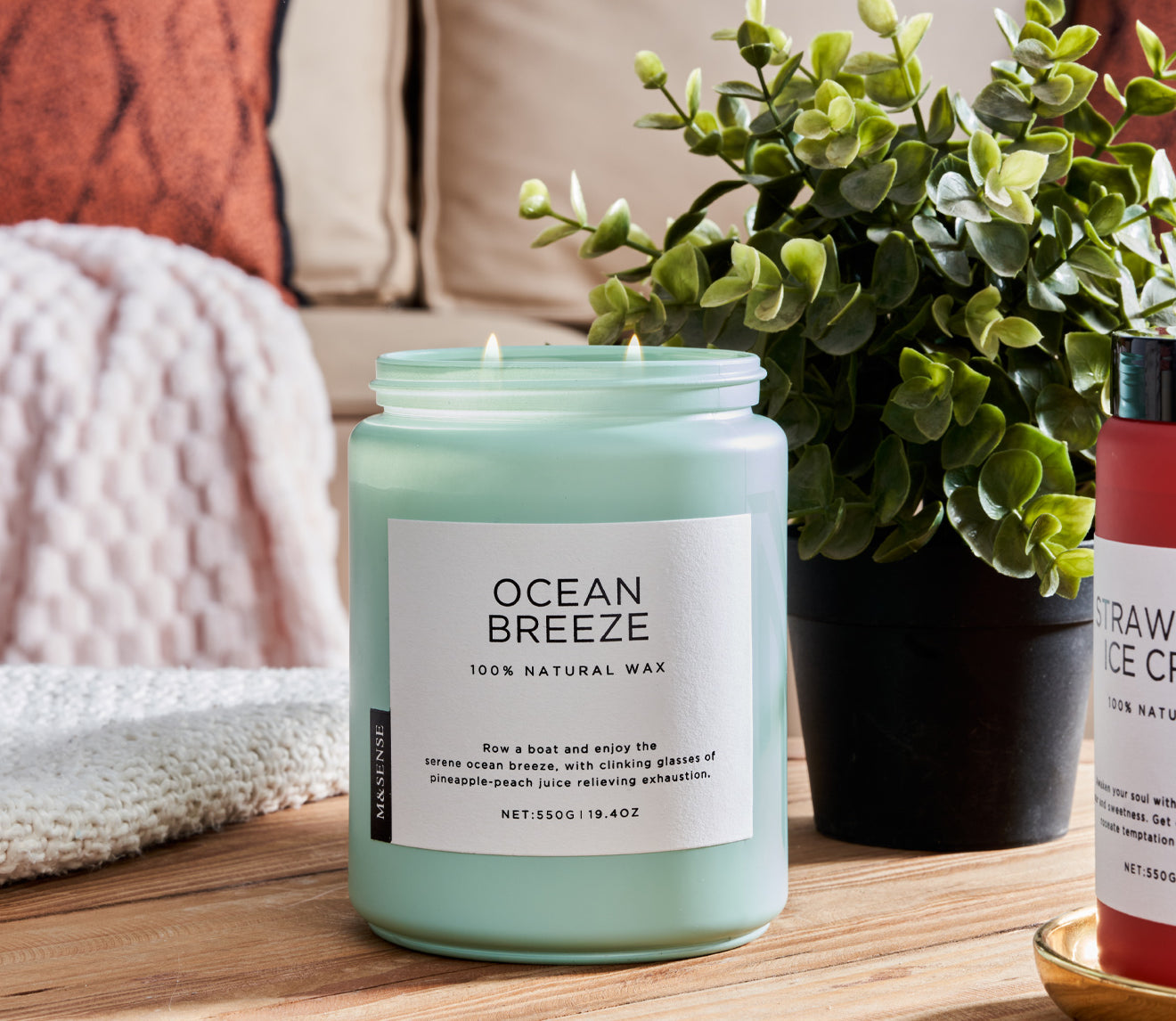 Ocean Breeze Coffee scented candle on a wooden table with a green plant, against a sofa background.