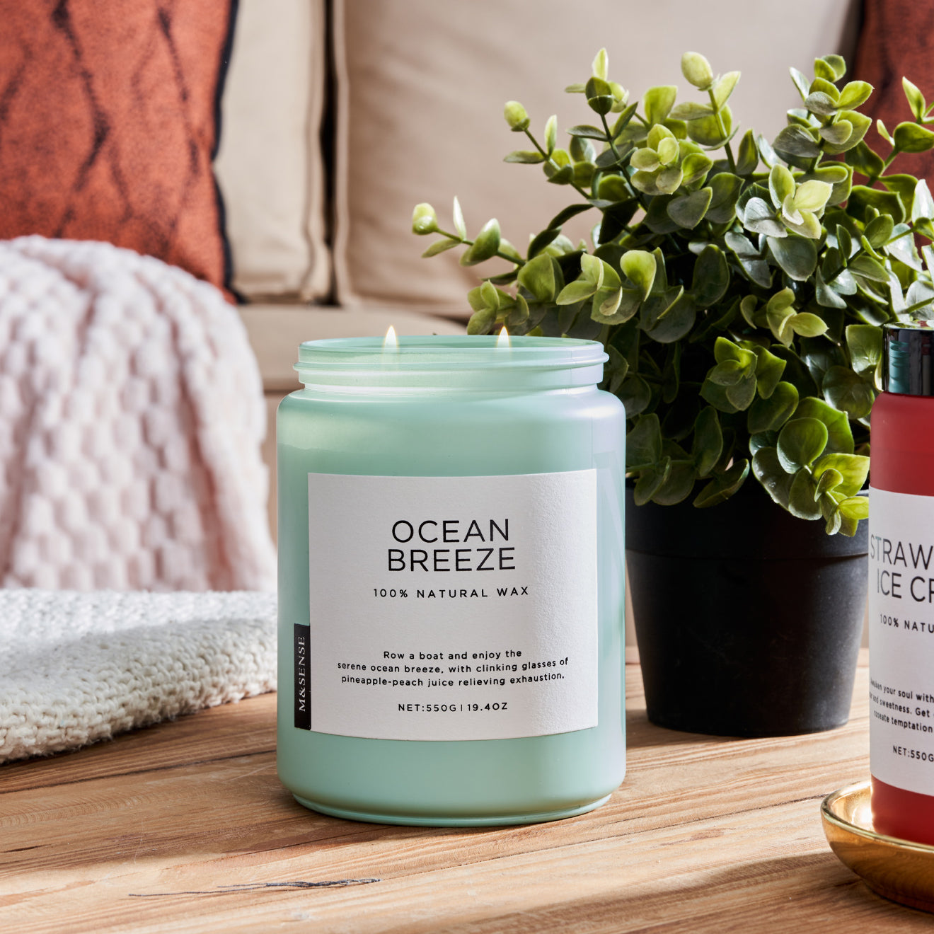 Ocean Breeze Coffee scented candle on a wooden table with a green plant, against a sofa background.