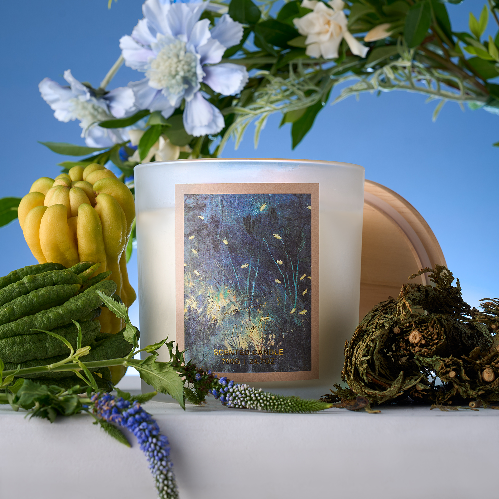 Candle with decorative label surrounded by flowers and plants on a blue background