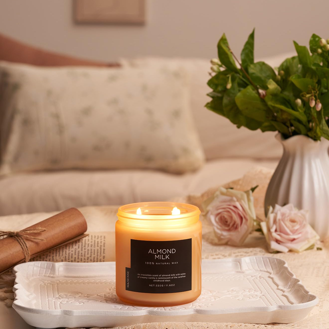 Candle labeled 'Almond Milk' on a tray with flowers and a couch in the background