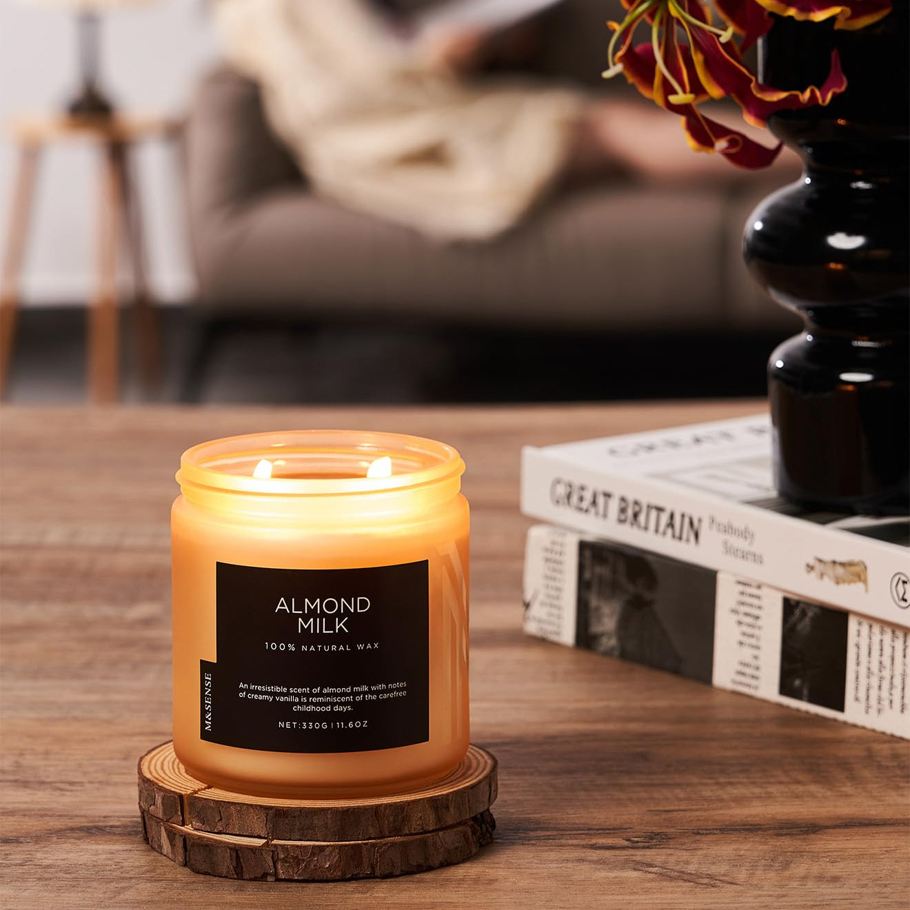 Candle labeled 'Almond Milk' on a wooden coaster with a blurred background of a cozy living room.
