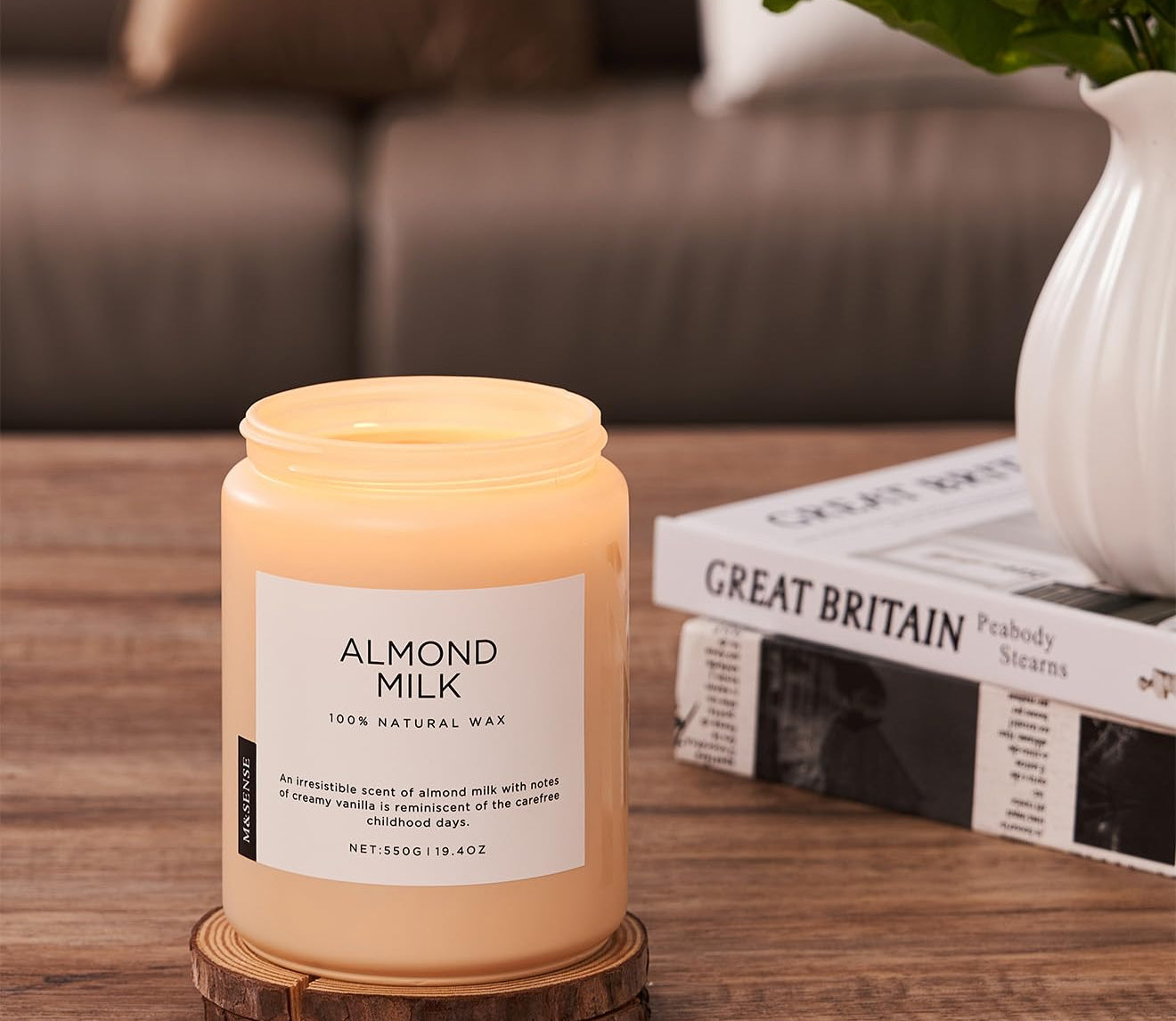 Candle labeled 'Almond Milk' on a wooden surface with a vase and books in the background.