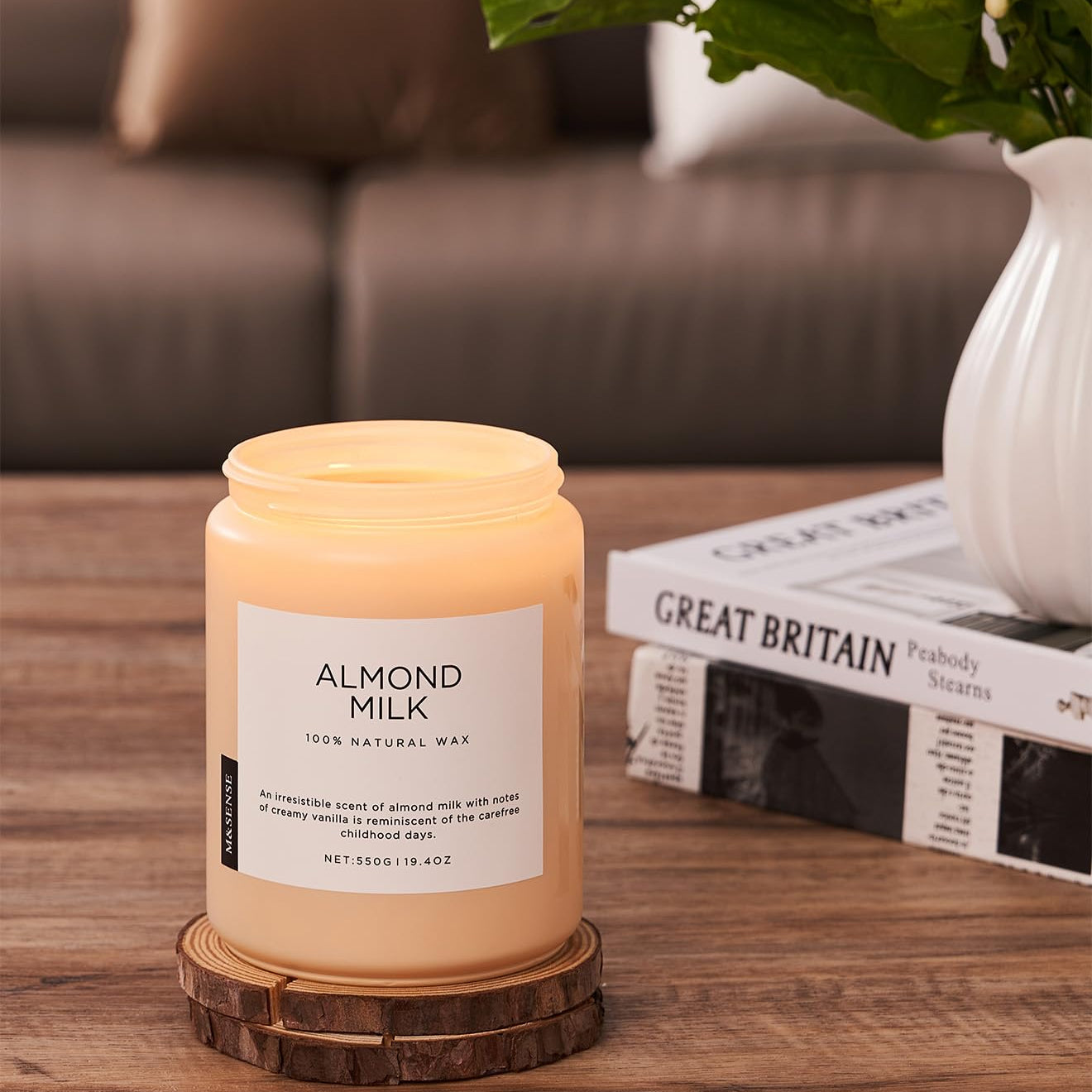 Candle labeled 'Almond Milk' on a wooden surface with a vase and books in the background.