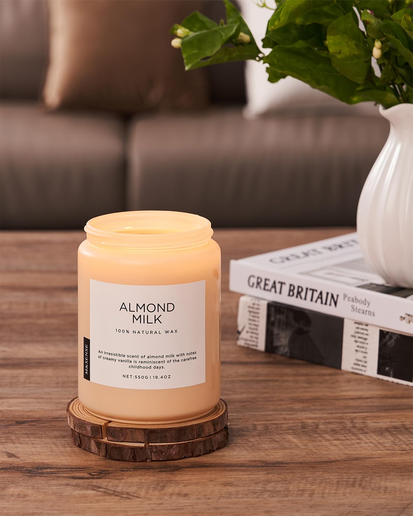 Candle labeled 'Almond Milk' on a wooden surface with a vase and books in the background.