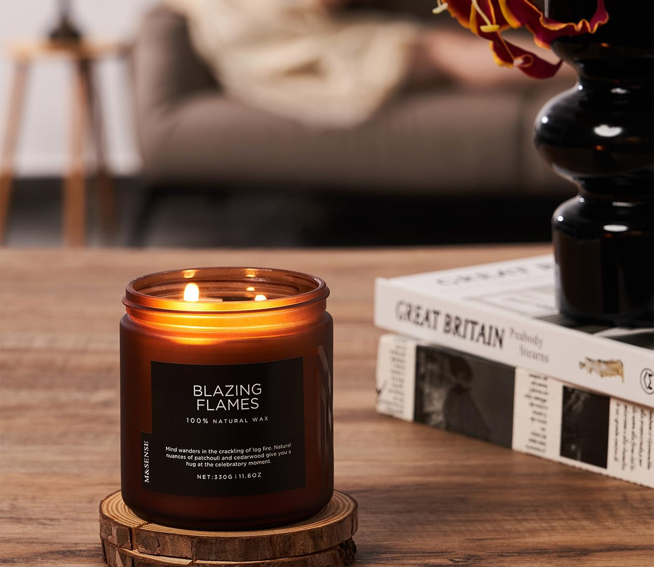 Candle labeled 'Blazing Flames' on a wooden coaster with a blurred background of a cozy living room.