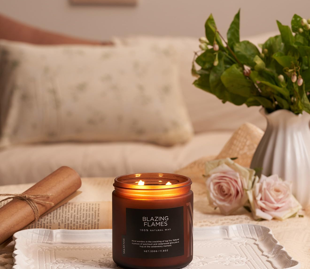 Candle labeled 'Blazing Flames' on a table with flowers and a vase in the background