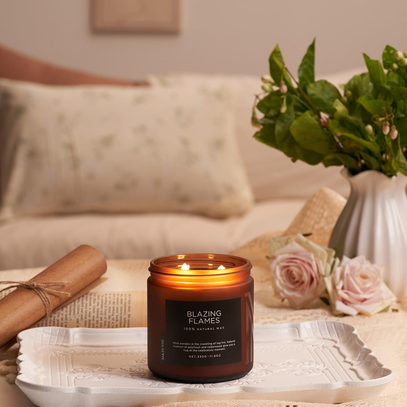 Candle labeled 'Blazing Flames' on a table with flowers and a vase in the background