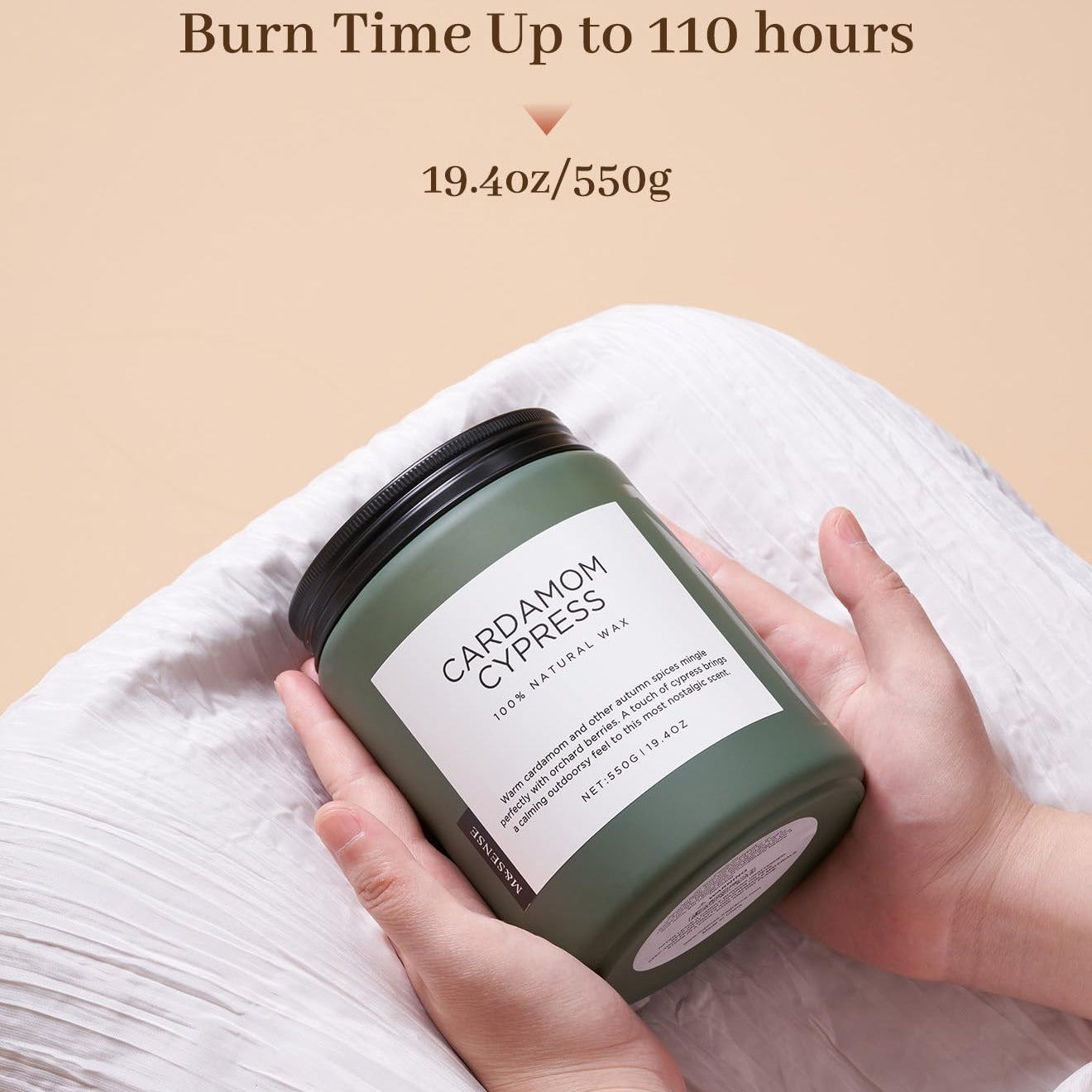 Hand holding a green candle labeled 'Cardamom Cypress' with text about burn time and weight on a beige background.