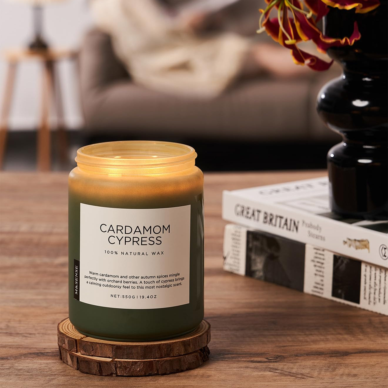 Cardamom Cypress candle on a wooden coaster with a blurred background of a living room.