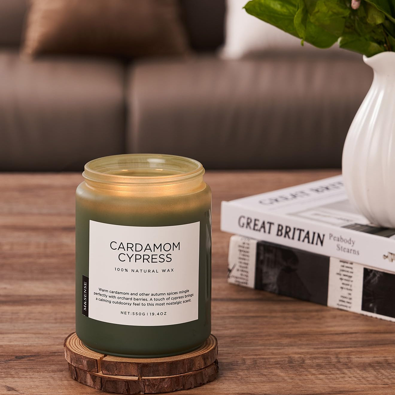 Candle labeled 'Cardamom Cypress' on a wooden coaster with a blurred background