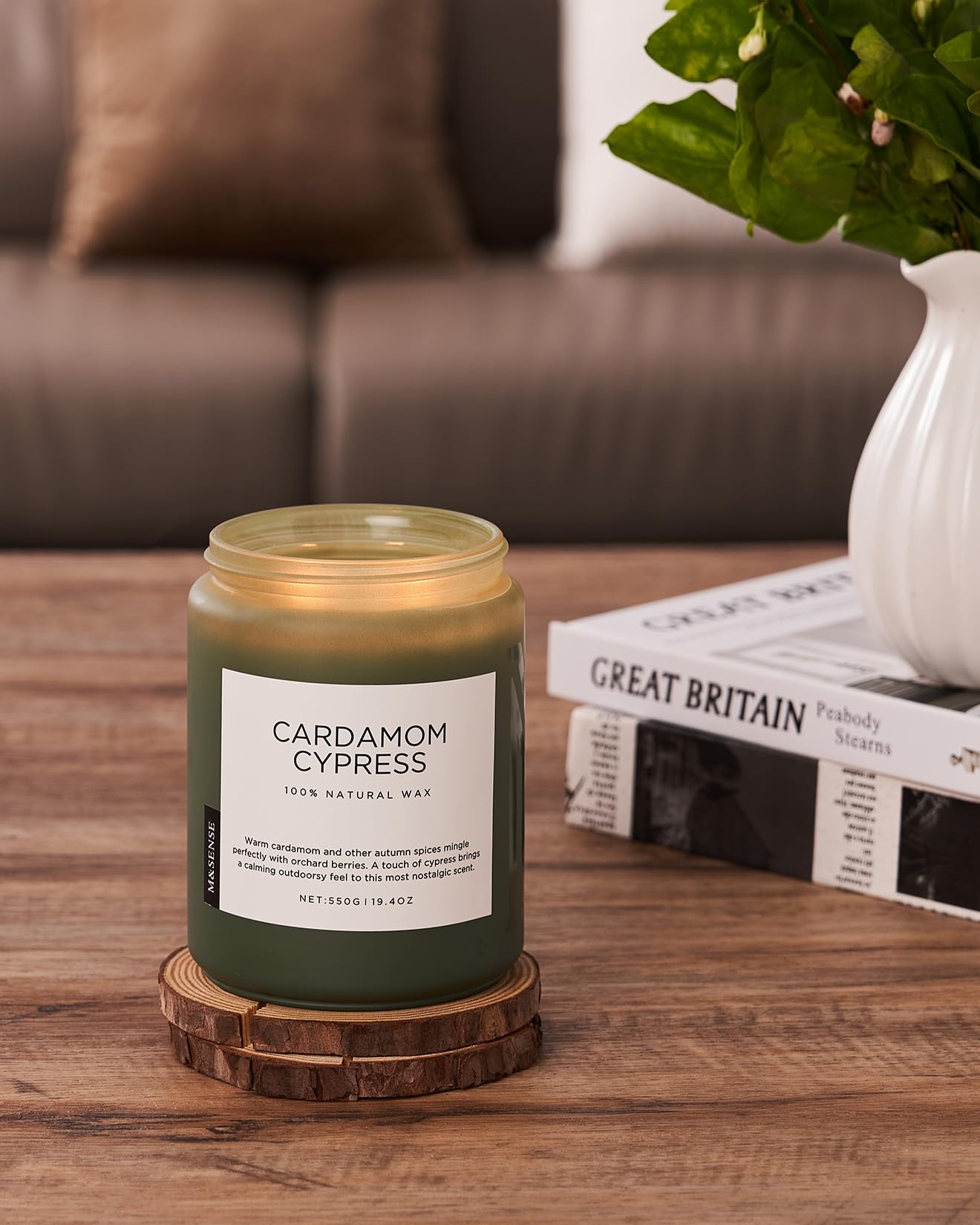 Candle labeled 'Cardamom Cypress' on a wooden coaster with a blurred background