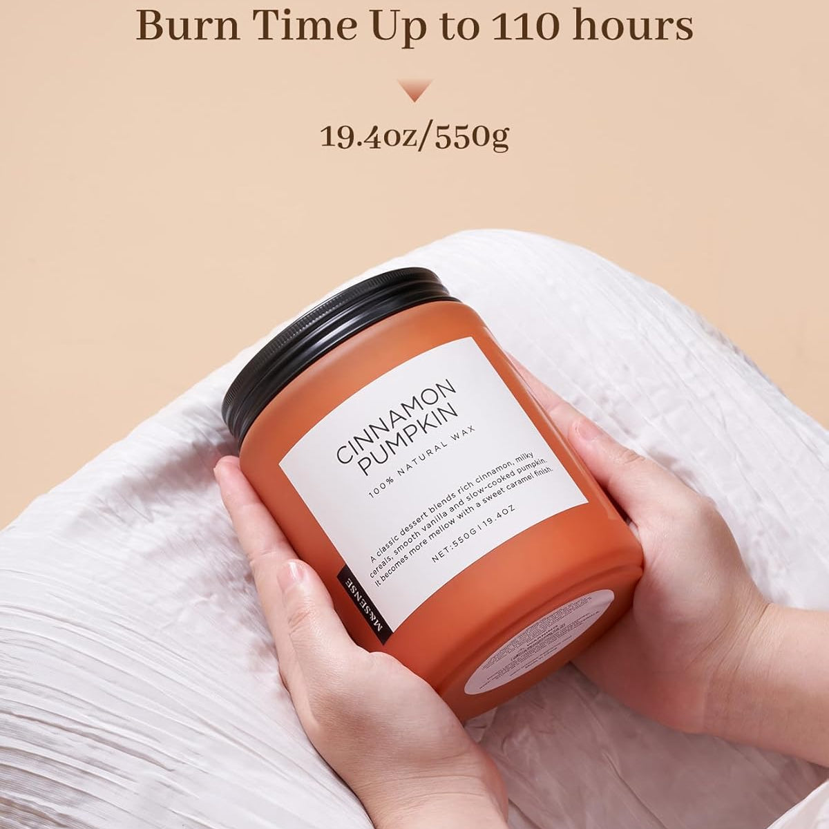 Candle labeled 'Cinnamon Pumpkin' held by a hand with a beige background