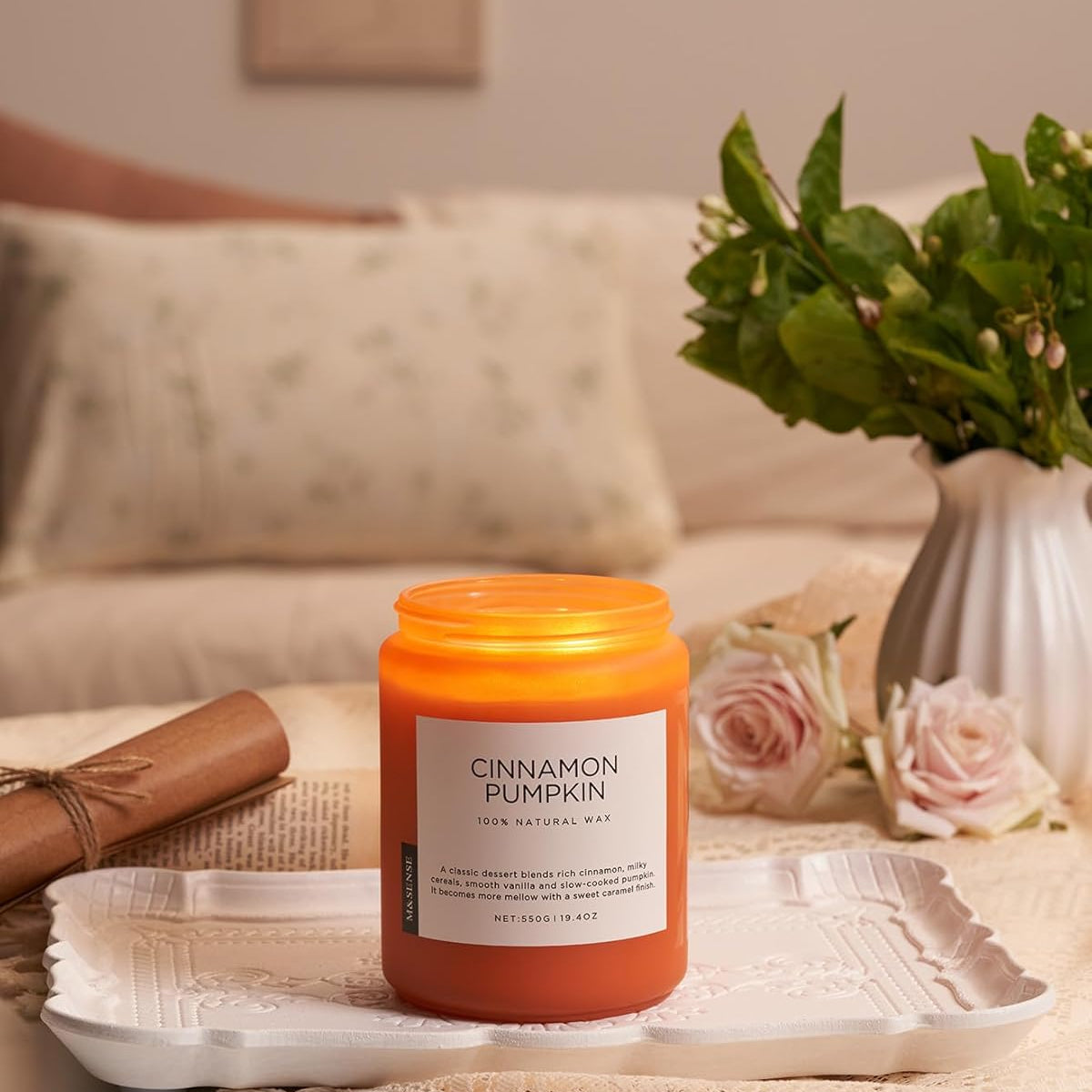 Cinnamon pumpkin candle on a table with a vase of flowers and a blanket in the background