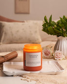 Cinnamon pumpkin candle on a table with a vase of flowers and a blanket in the background