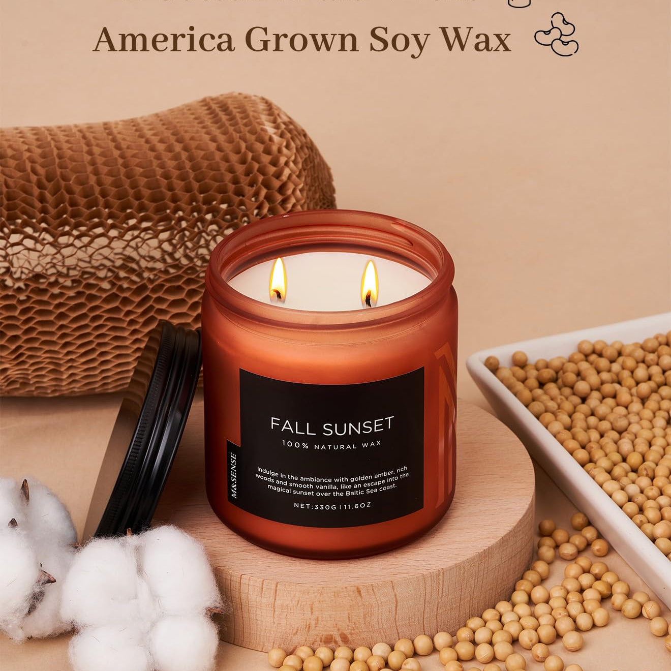 Candle with 'Fall Sunset' label on a wooden stand, surrounded by soybeans and cotton, with text about wicks and wax quality.