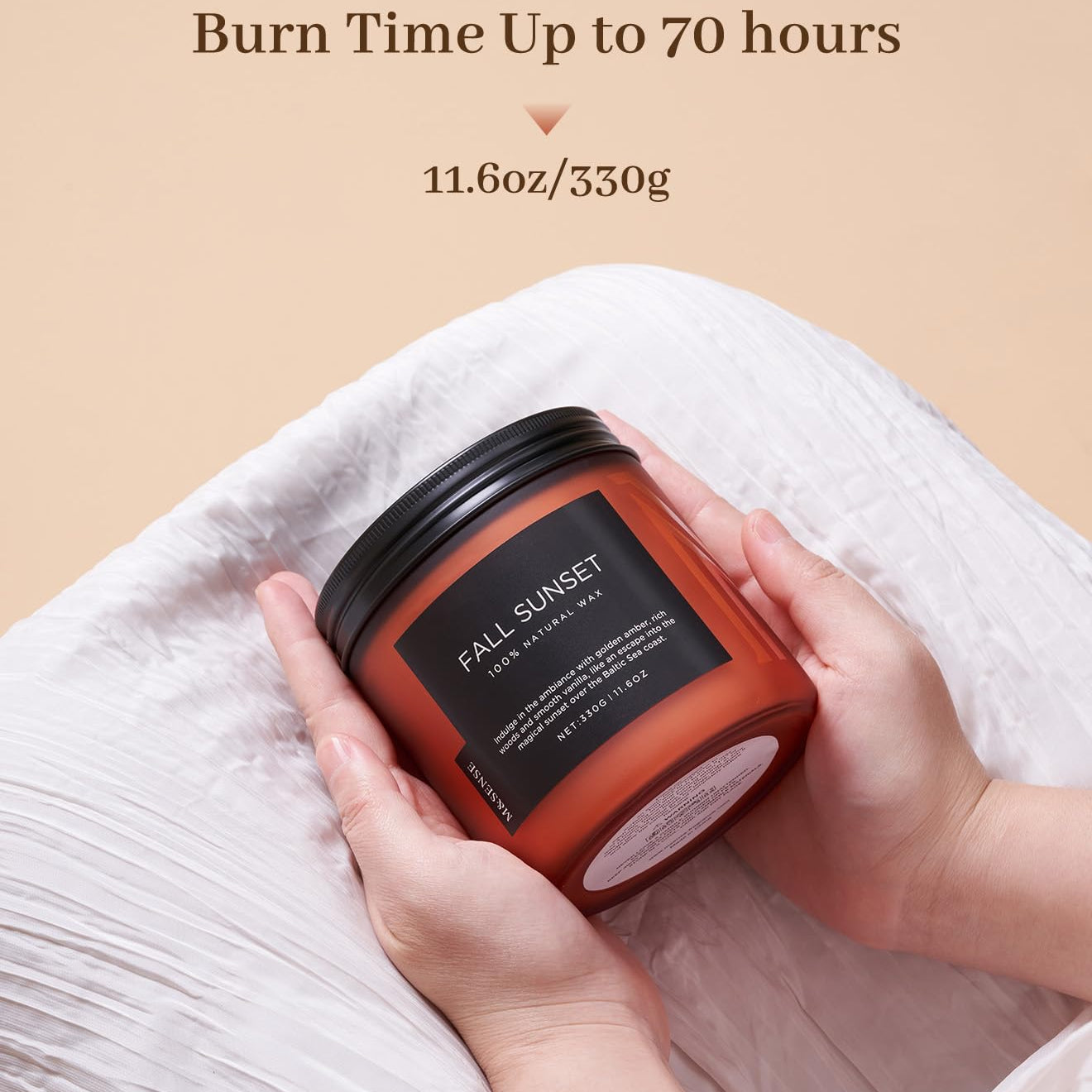 Candle labeled 'Fall Sunset' held by a hand with a beige background