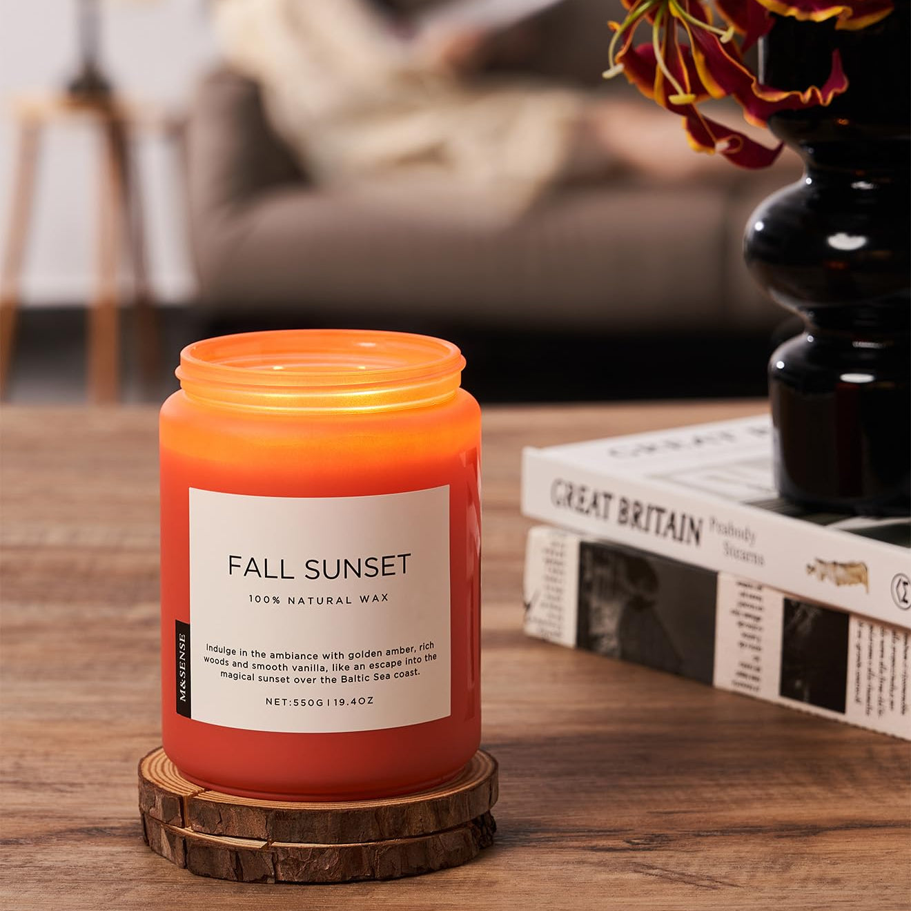 Candle labeled 'Fall Sunset' on a wooden coaster with a blurred background of a living room.