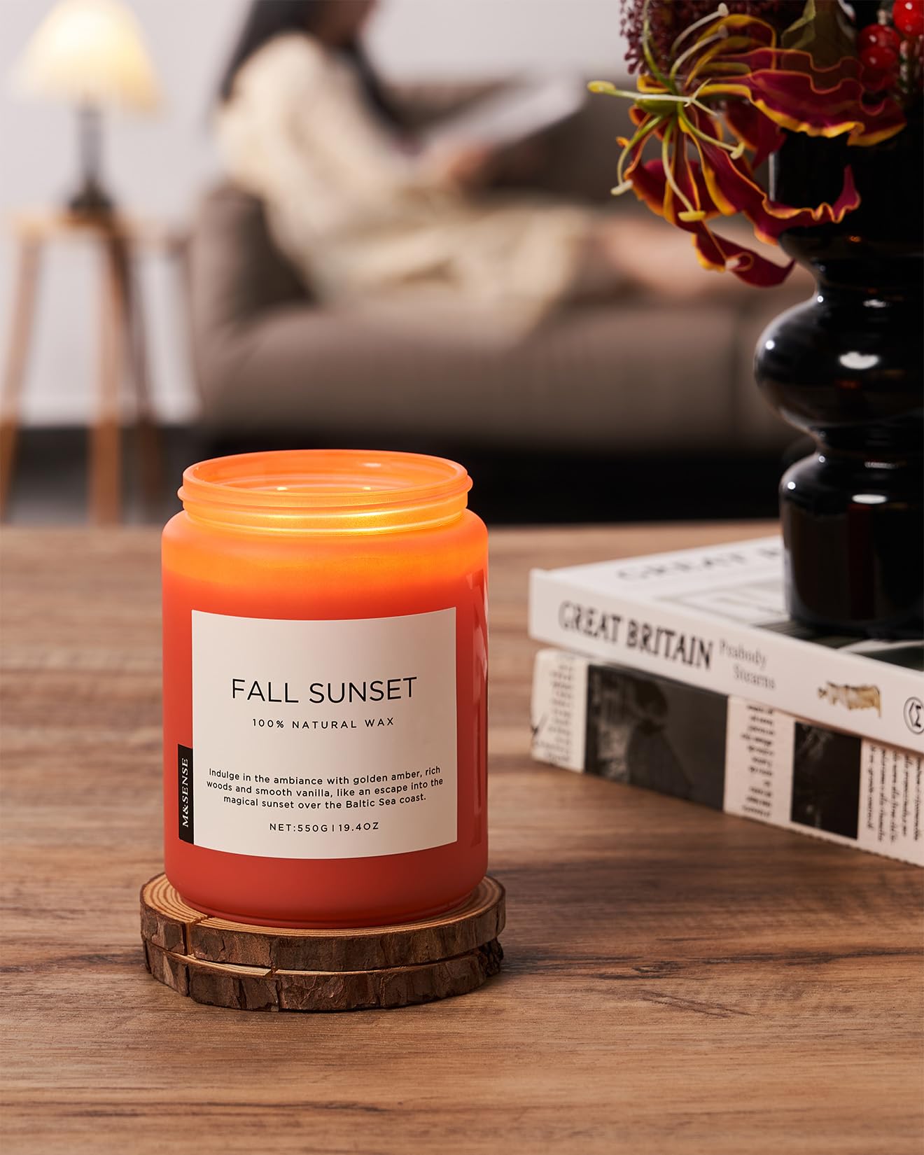 Candle labeled 'Fall Sunset' on a wooden coaster with a blurred background of a living room.