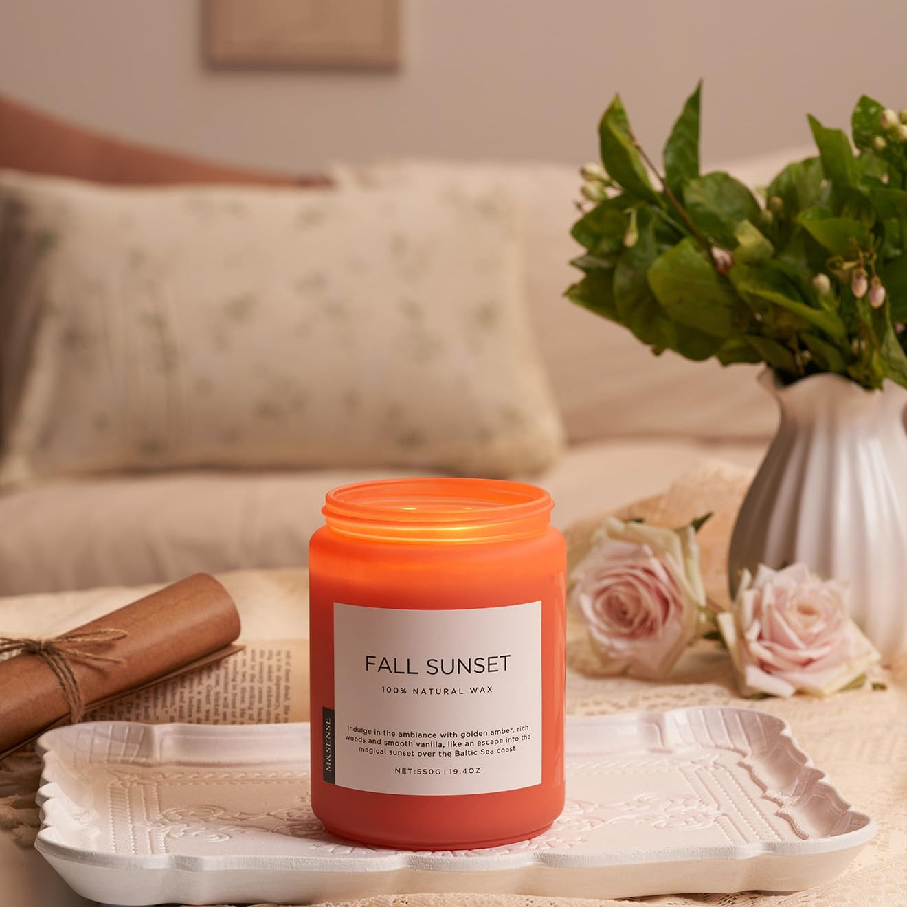 Candle labeled 'Fall Sunset' on a tray with flowers and a vase in the background