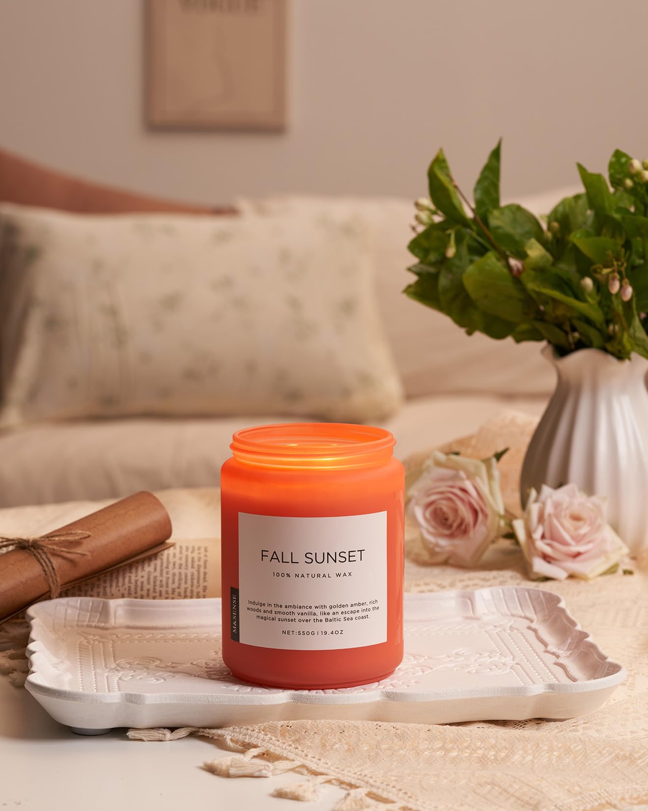Candle labeled 'Fall Sunset' on a tray with flowers and a vase in the background