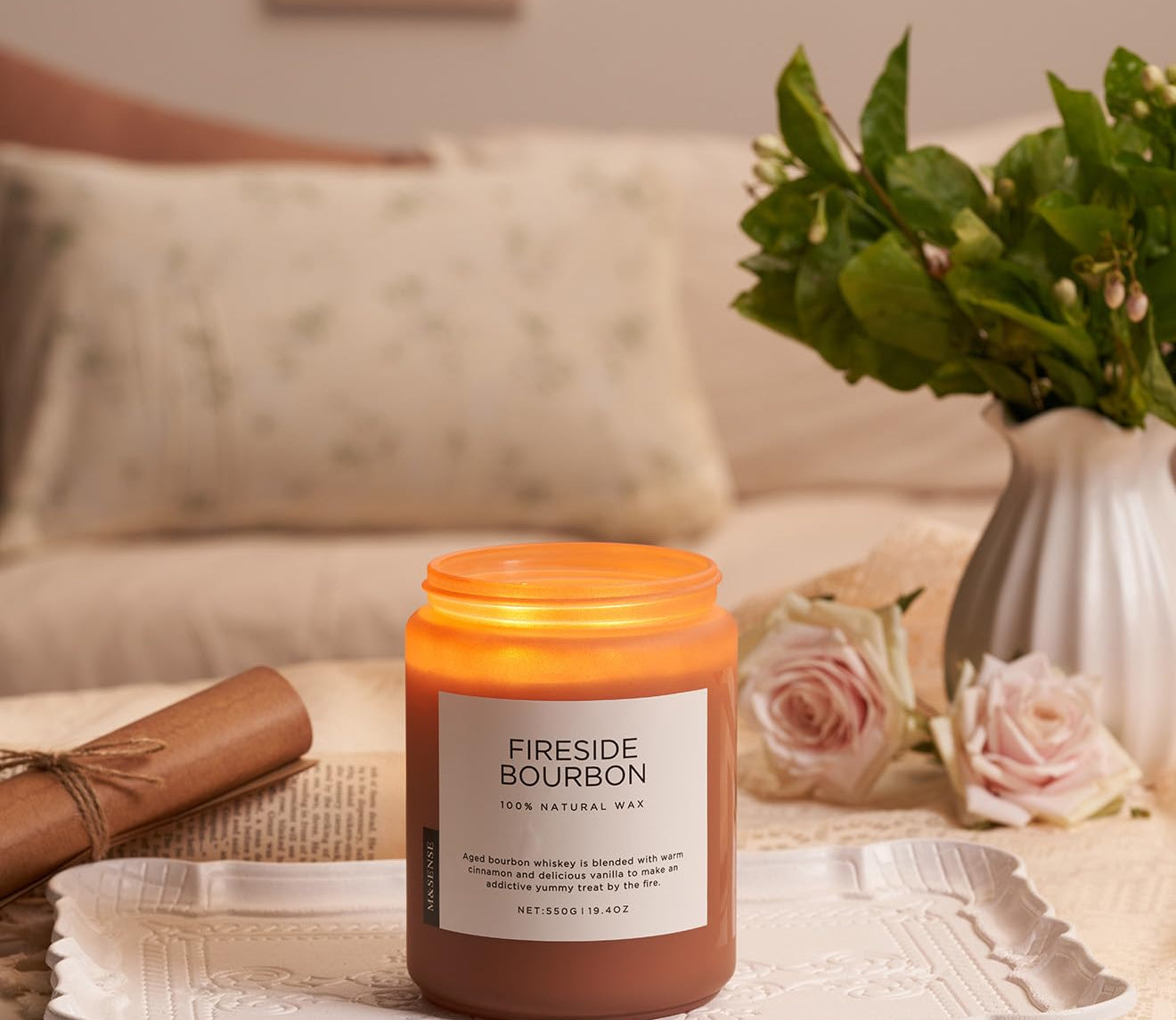 Candle labeled 'Fireside Bourbon' on a tray with a vase of flowers and a couch in the background.