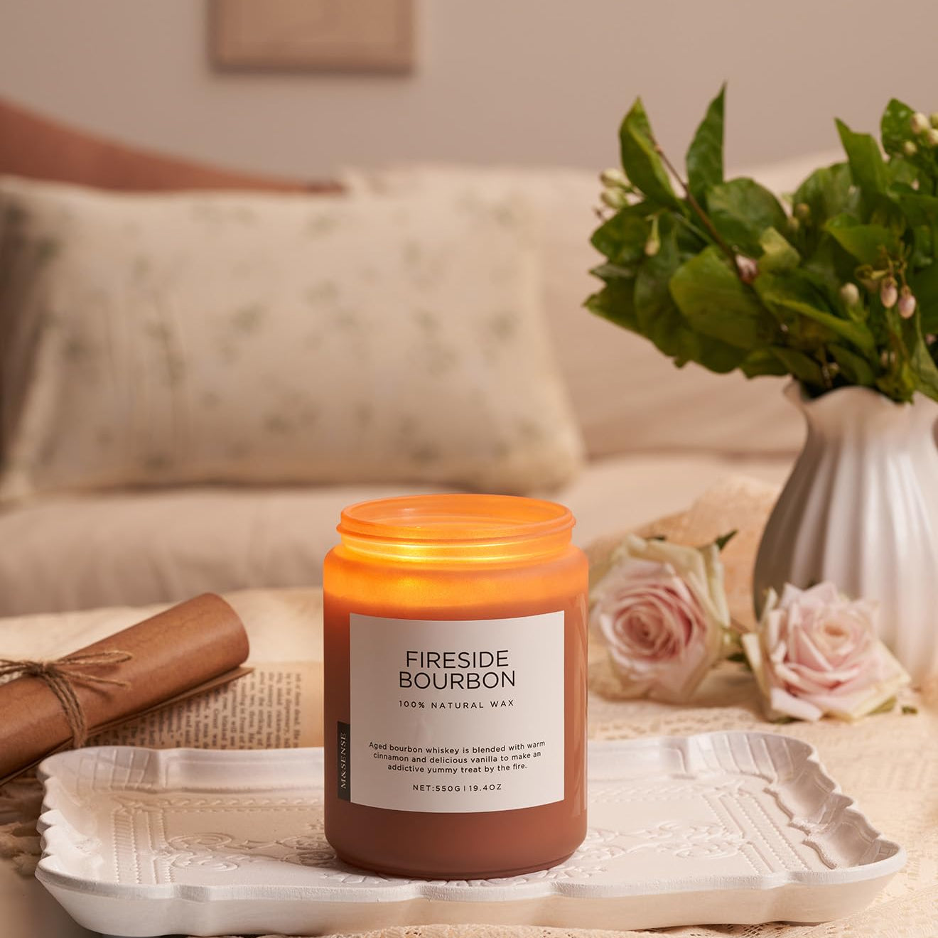 Candle labeled 'Fireside Bourbon' on a tray with a vase of flowers and a couch in the background.