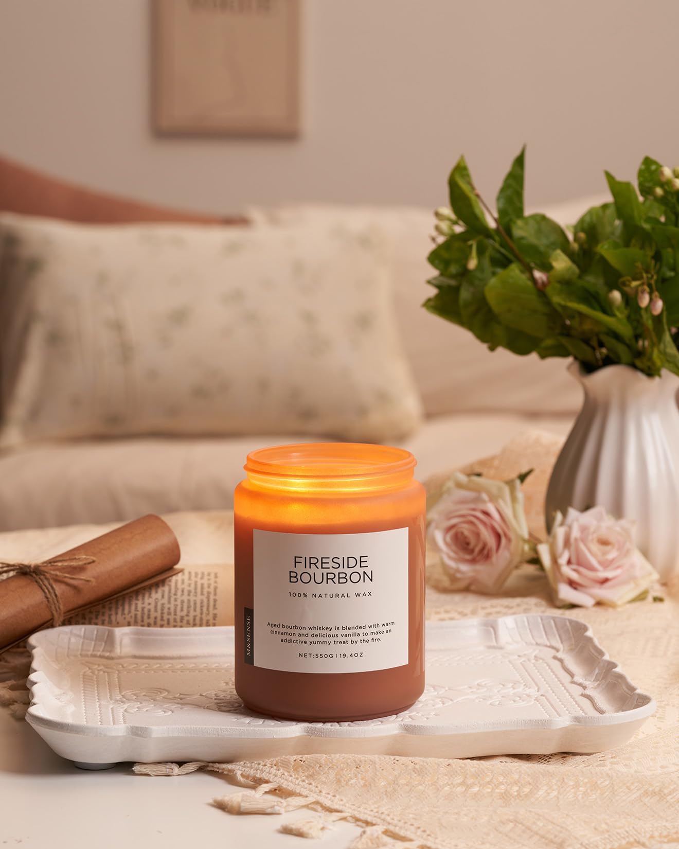 Candle labeled 'Fireside Bourbon' on a tray with a vase of flowers and a couch in the background.