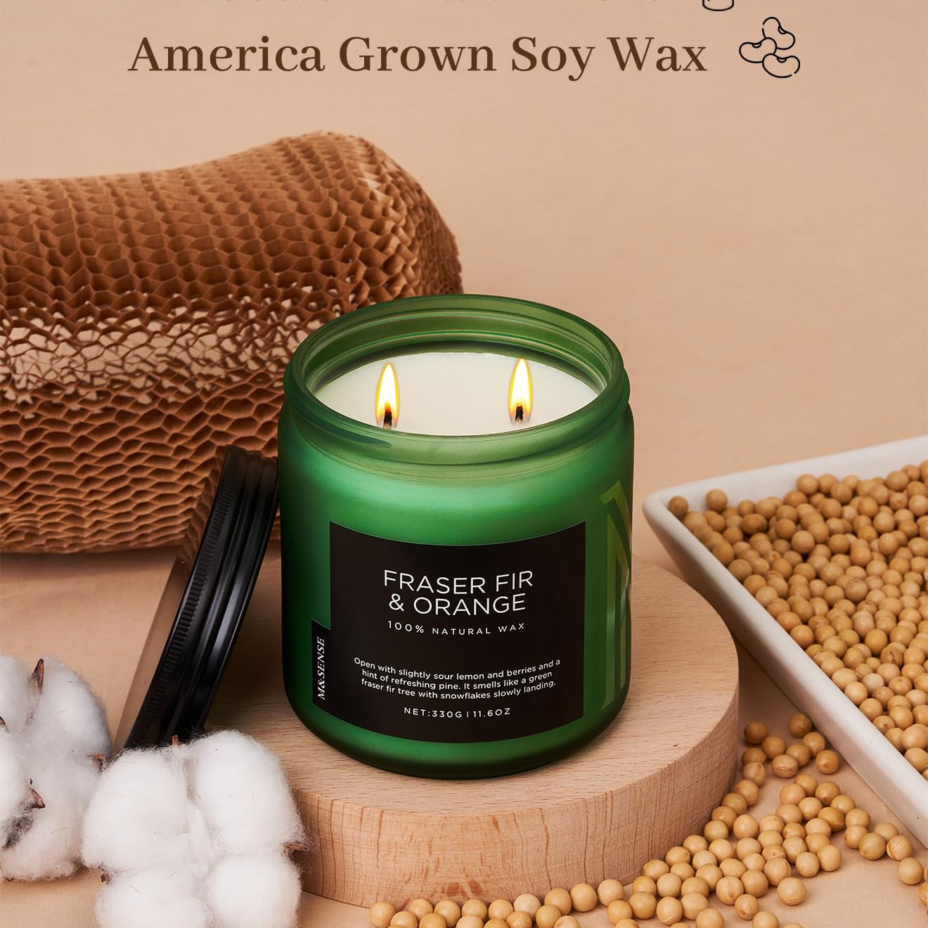 Green candle labeled 'Fraser Fir & Orange' with cotton, soybeans, and a woven basket on a beige background.