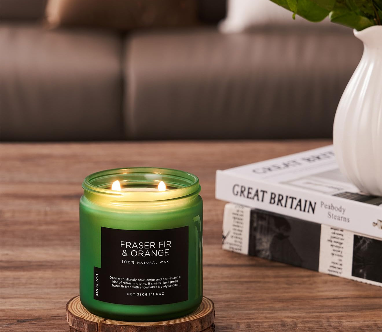 Green candle with a label on a wooden coaster in a living room setting.