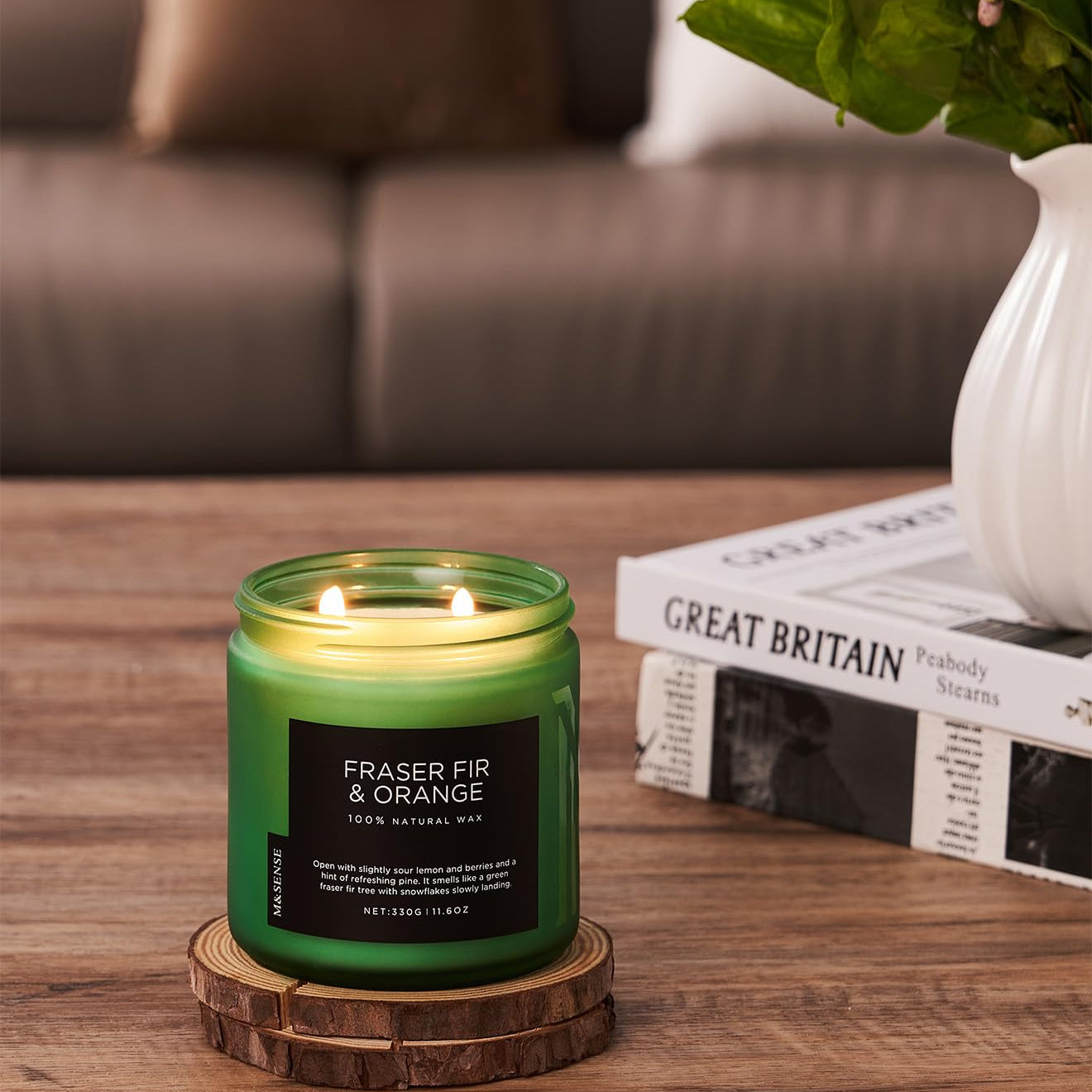 Green candle with a label on a wooden coaster in a living room setting.