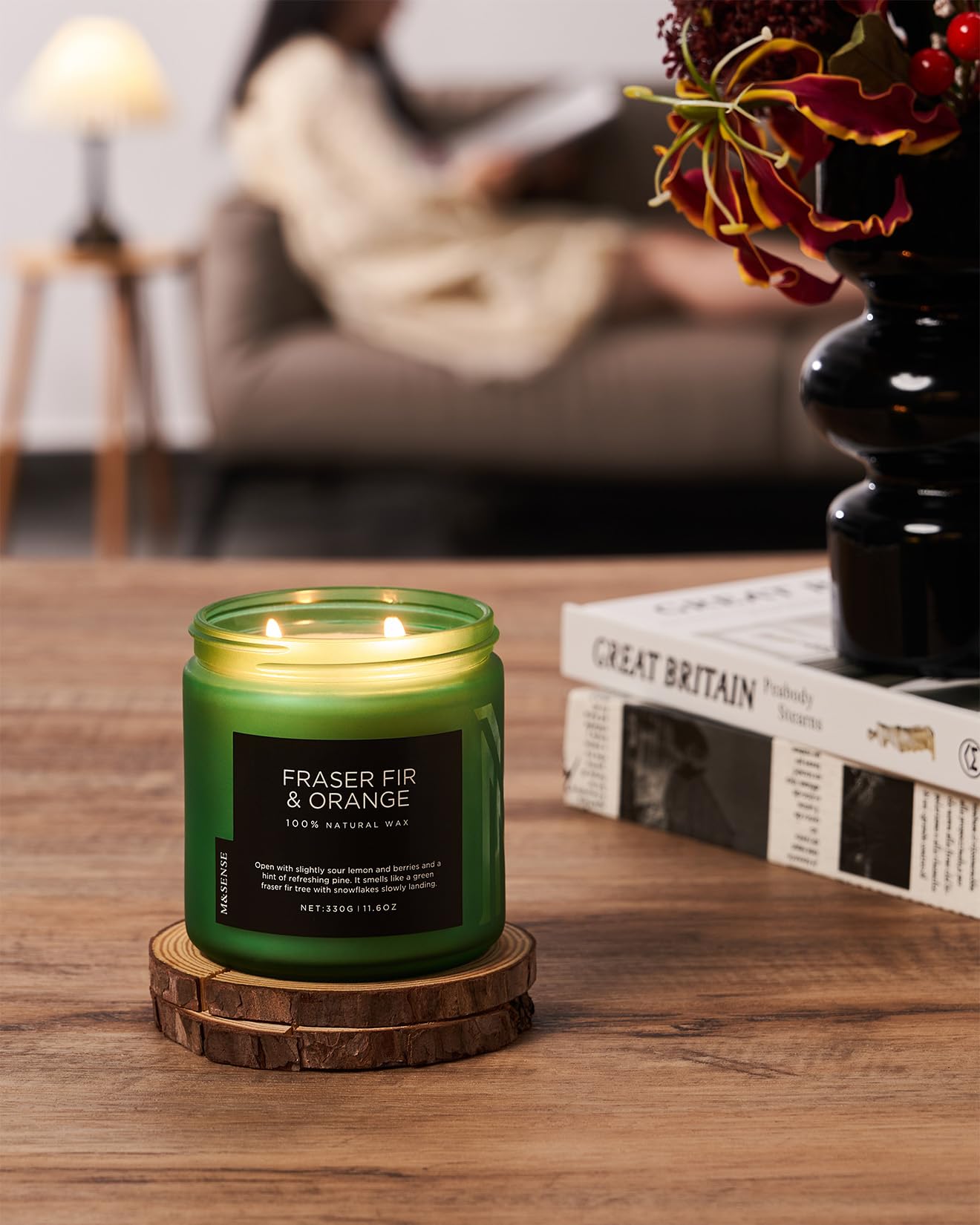 Green candle labeled 'Fraser Fir & Orange' on a wooden coaster with a blurred background of a cozy living room.