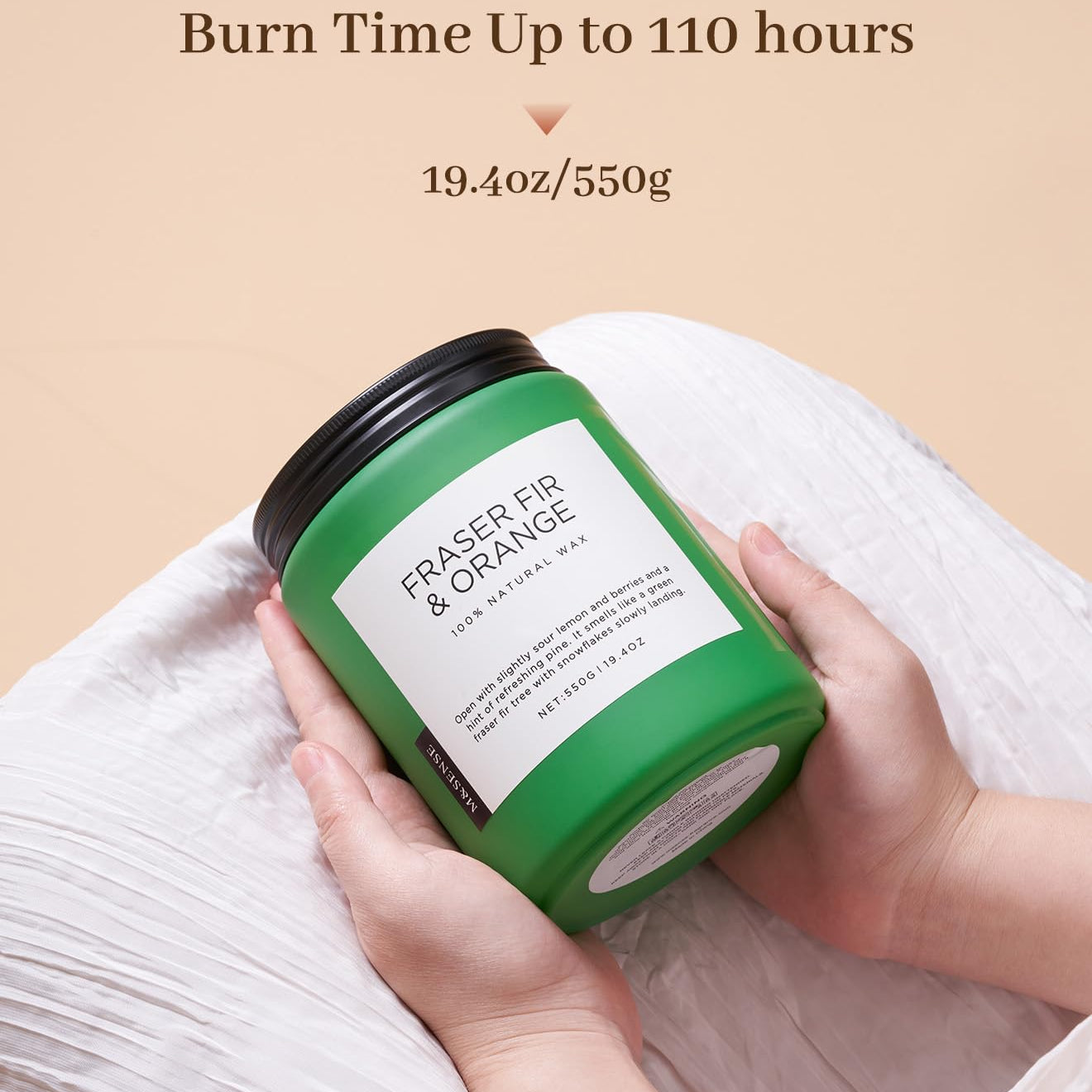 Green candle labeled 'Eraser Fir & Orange' held by a hand on a beige background with text about burn time.
