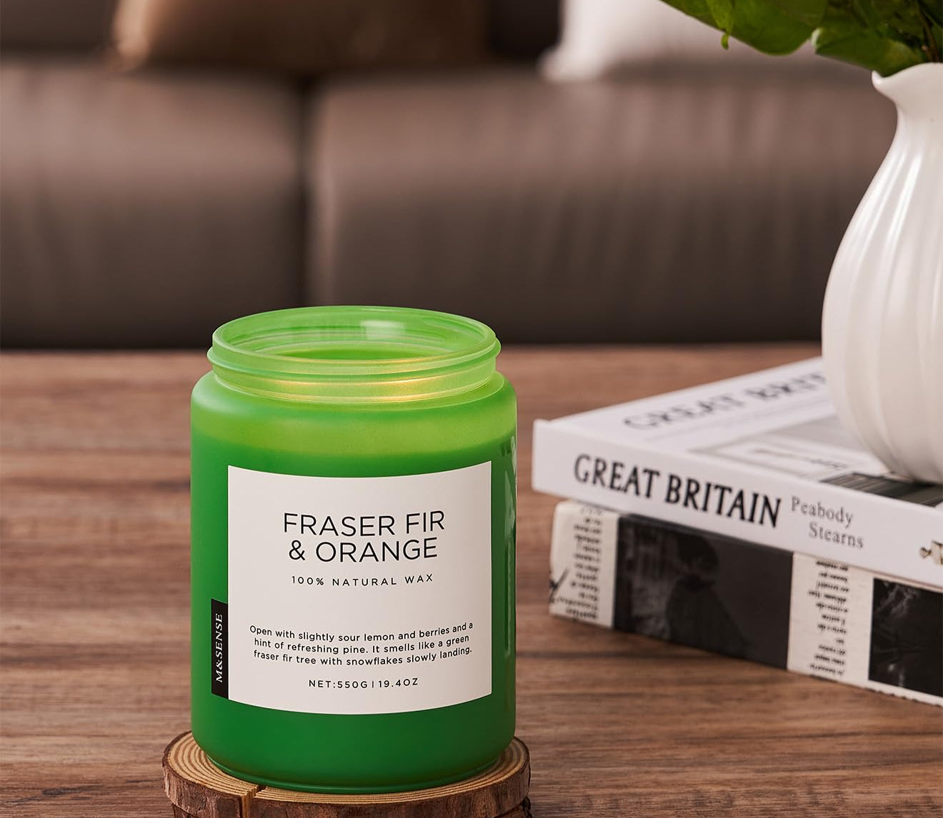Green candle labeled 'Fraser Fir & Orange' on a wooden coaster with a blurred background