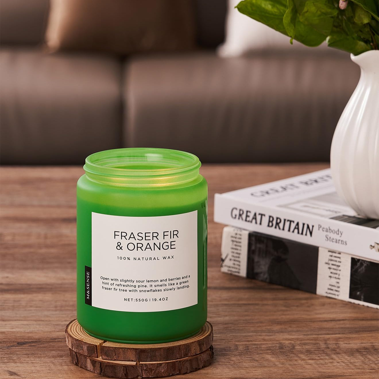 Green candle labeled 'Fraser Fir & Orange' on a wooden coaster with a blurred background