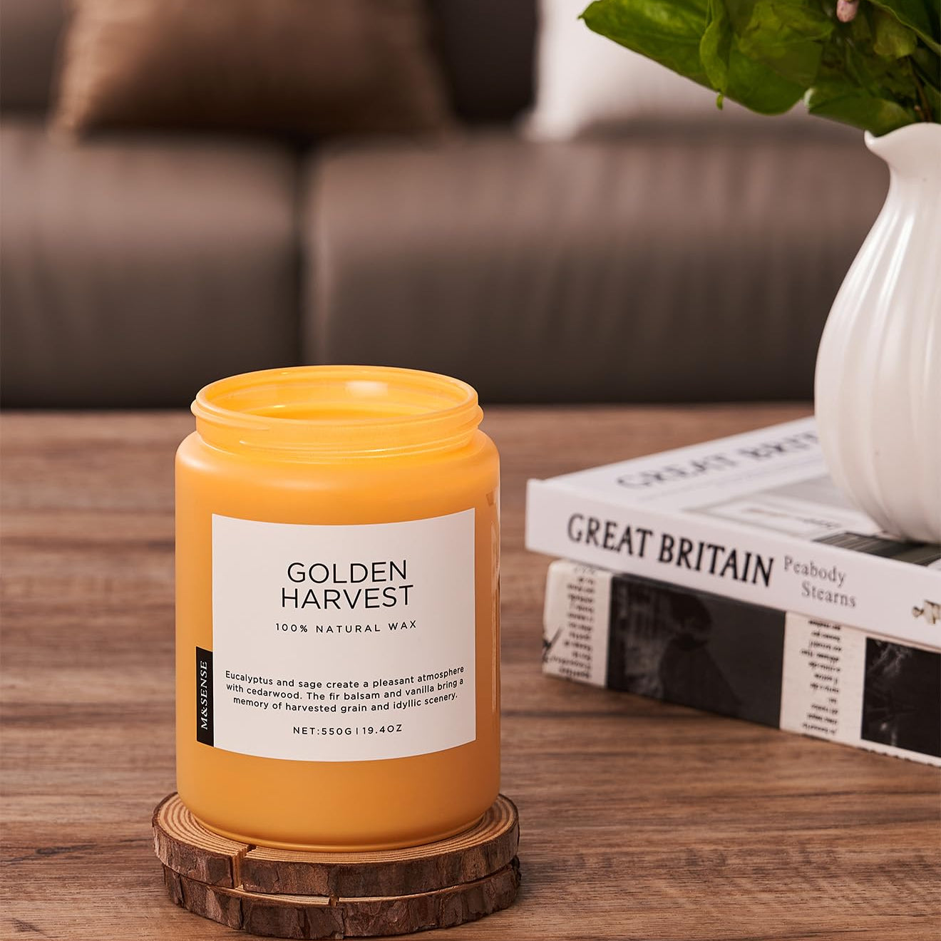Yellow candle labeled 'Golden Harvest' on a wooden coaster with a couch and plant in the background