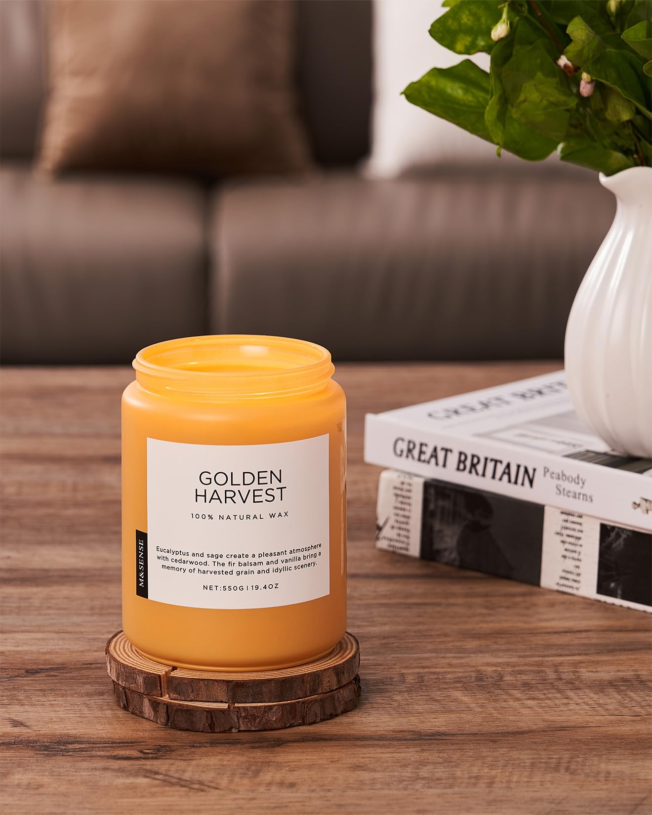 Yellow candle labeled 'Golden Harvest' on a wooden coaster with a couch and plant in the background