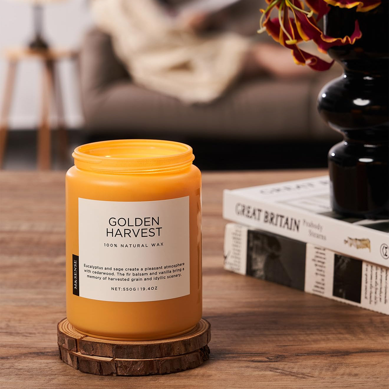 Yellow candle labeled 'Golden Harvest' on a wooden coaster with a blurred background of a cozy living room.