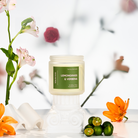 Candle labeled 'Lemongrass & Verbena' with flowers and limes on a blurred background