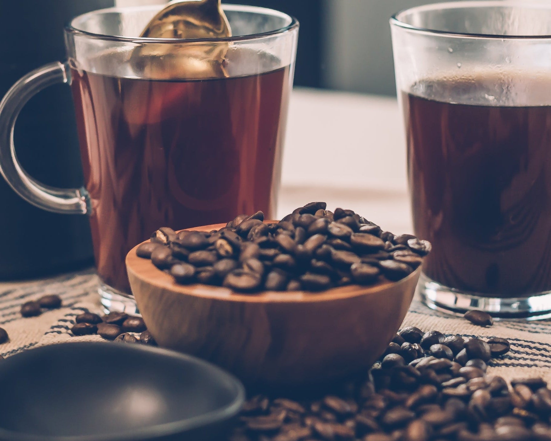 Person stirring a glass of iced tea with coffee beans on a table.