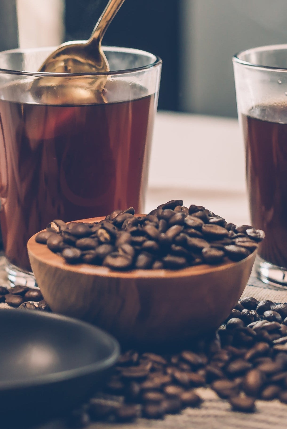 Person stirring a glass of iced tea with coffee beans on a table.