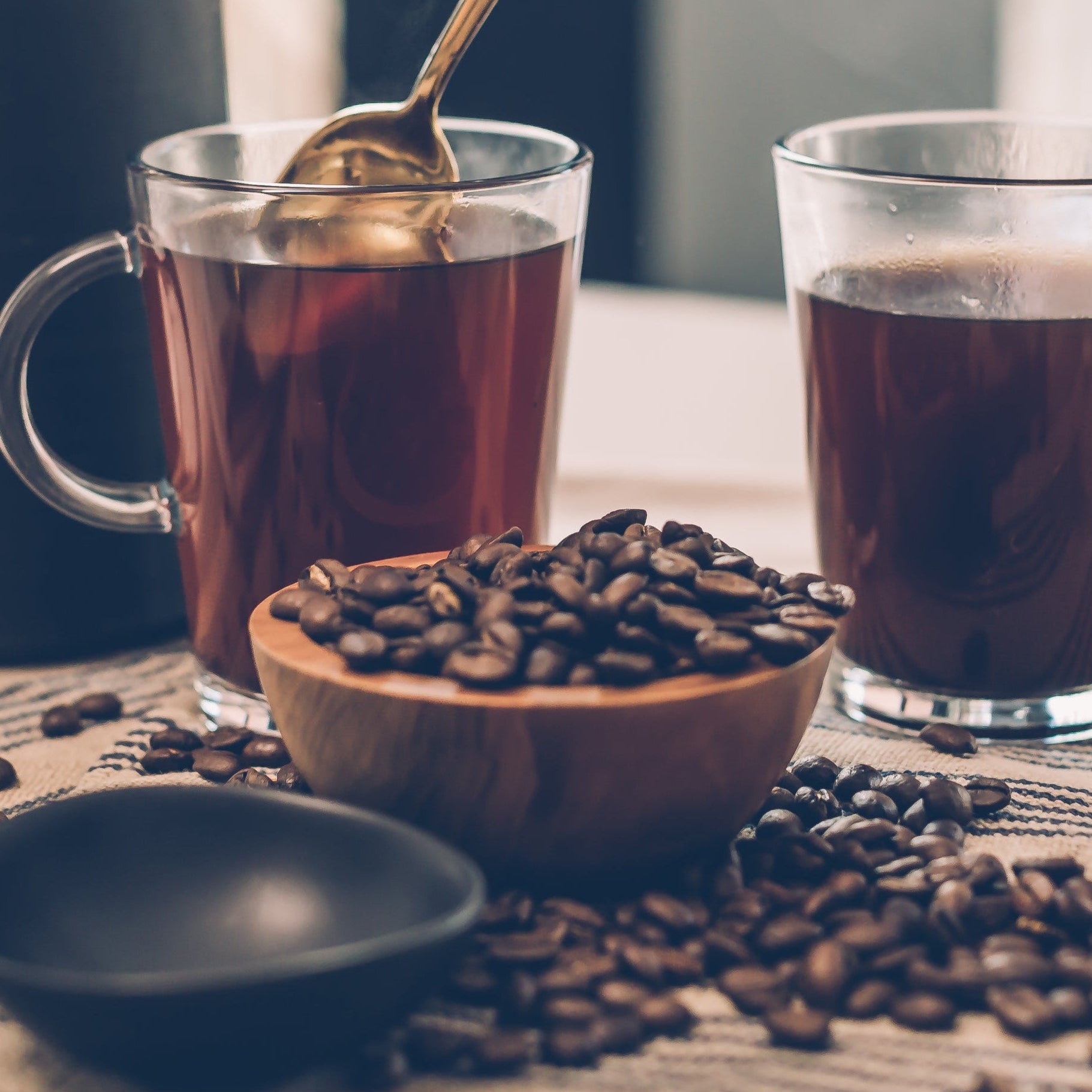Person stirring a glass of iced tea with coffee beans on a table.
